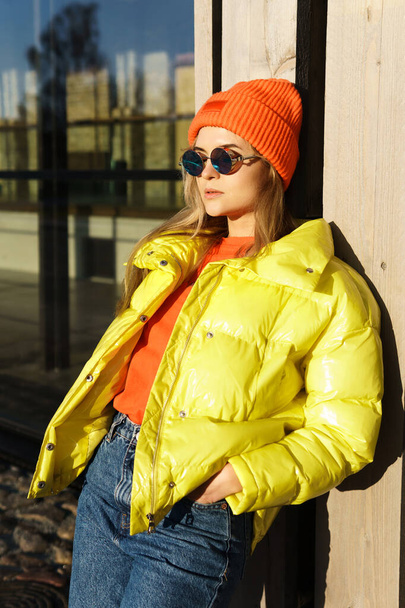 Portrait of  stylish girl wearing yellow puffer and orange knitted hat  - Fotó, kép