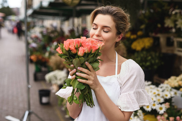 Young and beautiful woman florist with a heap of rose flowers in her little flower shop - Valokuva, kuva