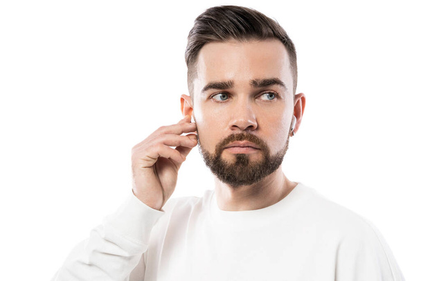 Portrait of handsome bearded man in white clothes  using wireless earbuds on white background - Fotó, kép