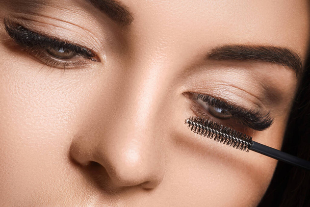 Close-up of female face and mascara wand for maximum volume of artificial eyelashes - 写真・画像