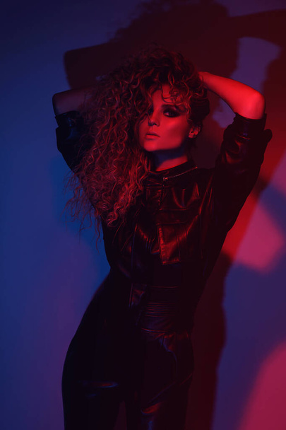 Young and sexy woman with a stylish Afro hairstyle wearing leather biker suit posing in colorful neon light - Foto, imagen