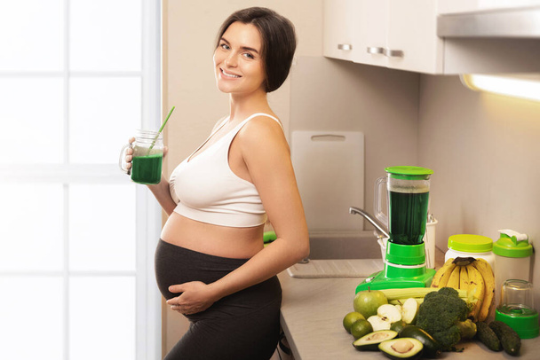 Young and happy pregnant woman drinking healthy green smoothie at home - Foto, Imagem