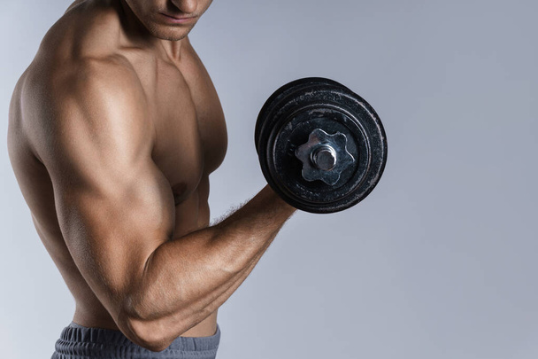 Young and muscular bodybuilder man working out with dumbbells on gray background - Foto, Bild
