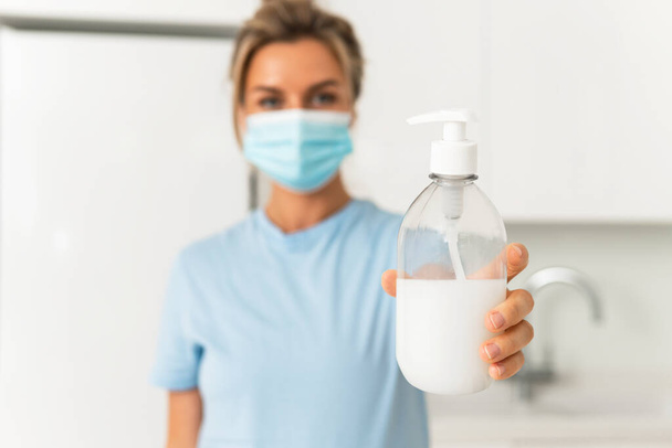 Woman wearing prevention mask is using hand sanitizer or liquid soap for hands disinfection at home - Foto, Bild