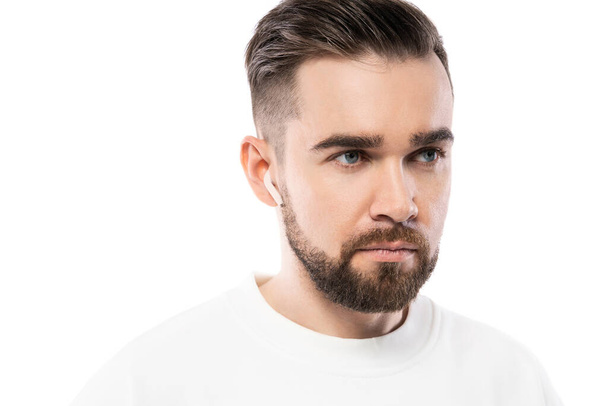 Portrait of handsome bearded man in white clothes  using wireless earbuds on white background - Photo, image