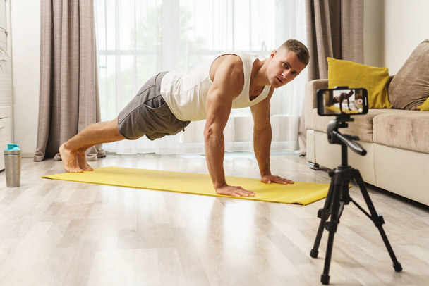 Fitness blogger is streaming or recording video for his subscribers during his home workout - Foto, Bild