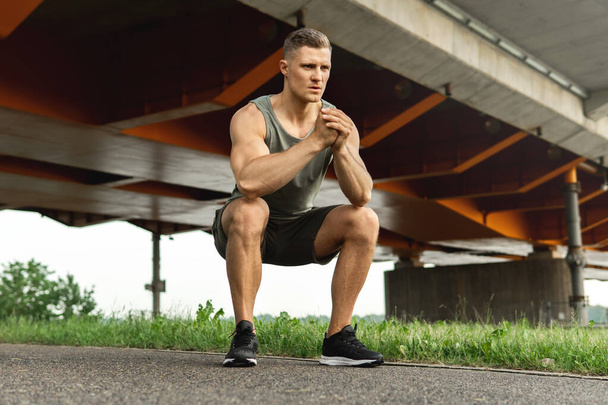 Young and muscular man is making squats under the bridge during his street workout - Foto, immagini