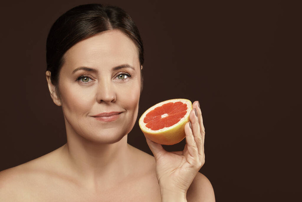 Beautiful and happy middle aged woman with a grapefruit in her hand. Concept of natural cosmetics and skin care. - Photo, image