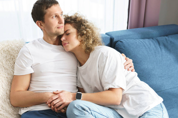 Young and happy couple sitting on a sofa and relaxing at home - Foto, Imagem