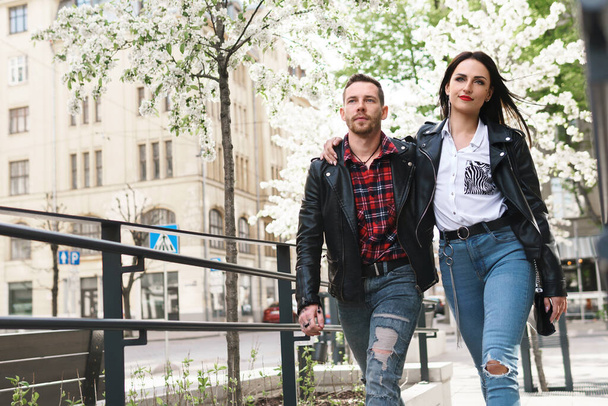 Confident people in relationship. Young and beautiful couple in love wearing leather jackets walking on a city street during their date. - Photo, Image