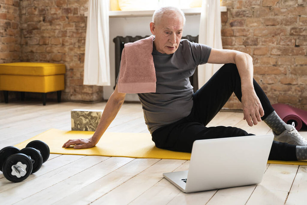 Active elderly man watching online fitness class during his home workout - Фото, зображення