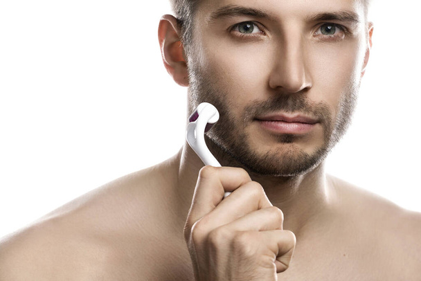 Young handsome man is using derma roller for beard growth on white background - Foto, Bild