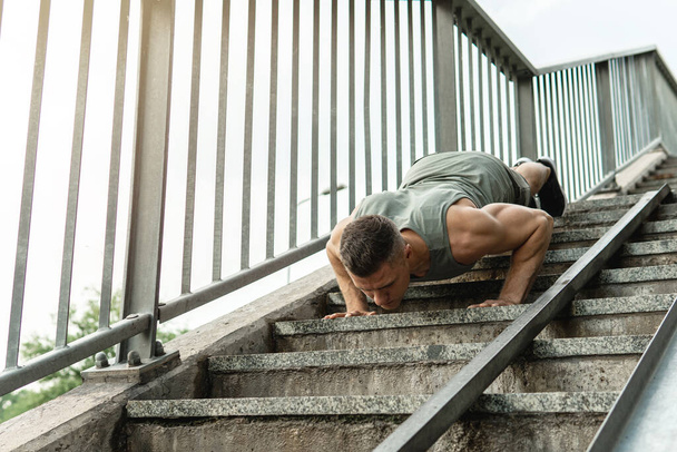 Young and muscular man is doing push-ups during calisthenic workout on a street - Foto, Bild