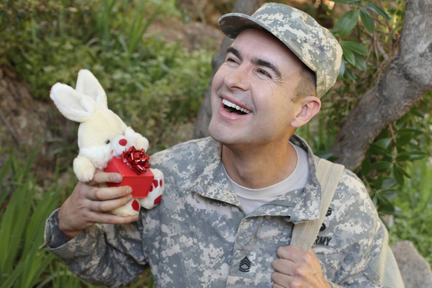 close-up portret van knappe jonge soldaat met speelgoed konijn en geschenkdoos buiten - Foto, afbeelding