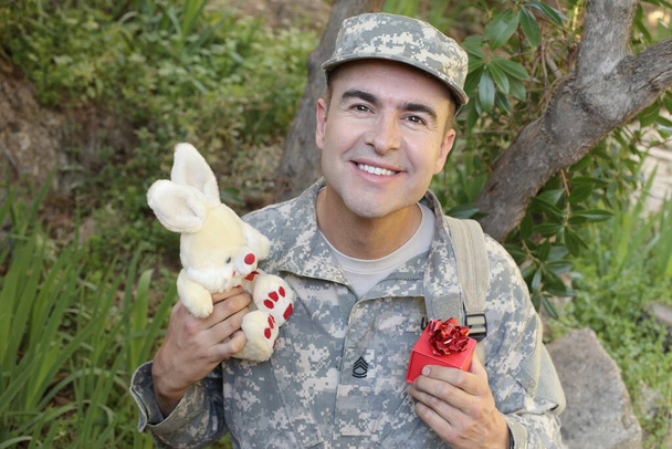 zblízka portrét pohledného mladého vojáka s hračkou králíčka a dárkové krabice venku - Fotografie, Obrázek
