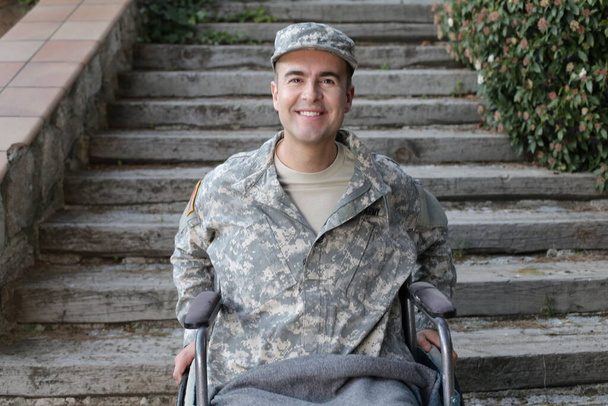 駐車場の階段前の車椅子に座る制服姿のハンサムな若い兵士のクローズアップ肖像画 - 写真・画像