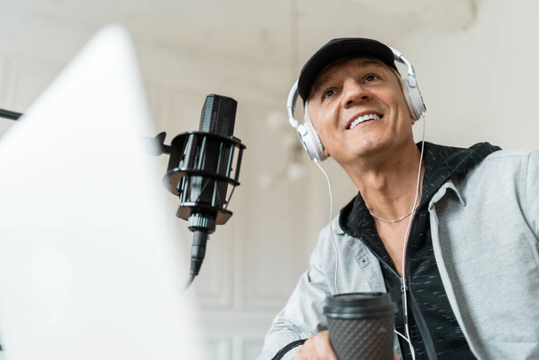 A blogger communicates with people through a microphone. Portrait of a fashionable radio host pro age man working in a recording studio. - Foto, immagini