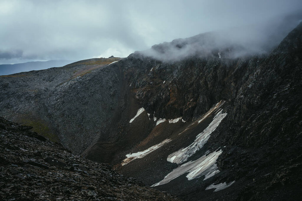 Dark atmospheric landscape on edge of abyss in highlands. Dangerous mountains and abyss in overcast weather. Danger mountain pass and sharp rocks among low clouds. Dangerous rainy weather in mountains - Photo, image