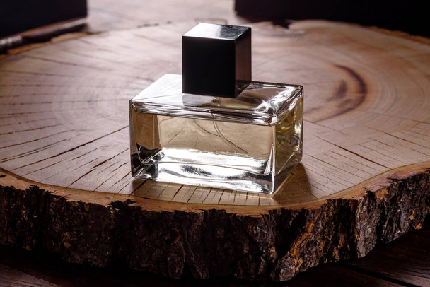 Glass perfume bottle with rosemary sprig on wooden podium illuminated with hard light - Fotó, kép
