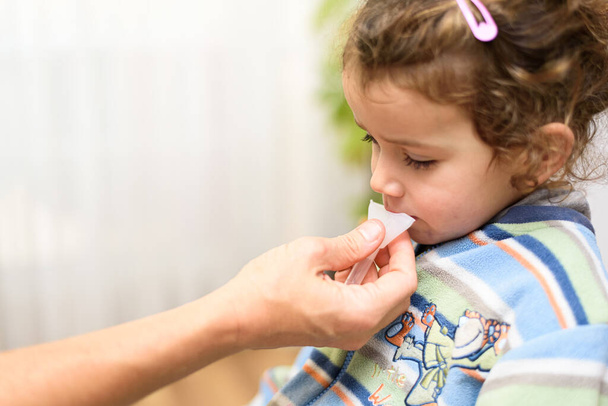 Una niña de tres años escupe en un tubo de prueba de saliva para antígenos covid19. - Foto, Imagen