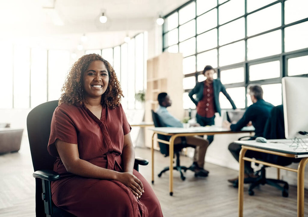 La positividad es la clave del éxito. Retrato de una joven empresaria sentada en una oficina moderna con sus colegas trabajando en segundo plano. - Foto, Imagen