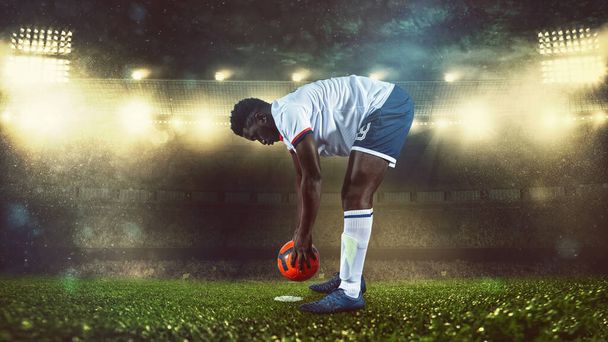 Cena de futebol à noite jogo com o jogador em branco e uniforme colocando a bola para chutar - Foto, Imagem