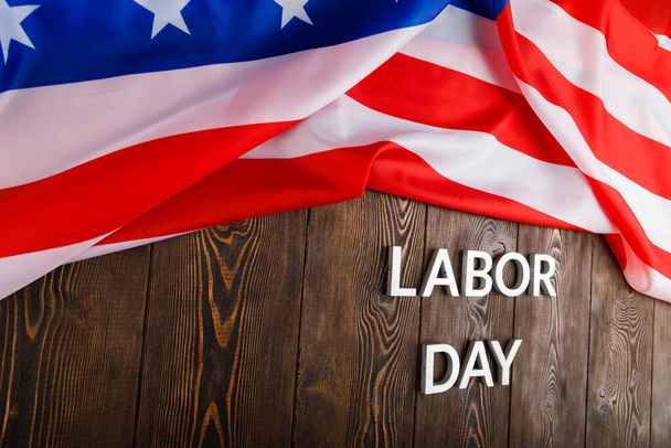 words labor day laid with silver metal letters on wooden surface with crumpled USA flag on left side - Foto, Imagem