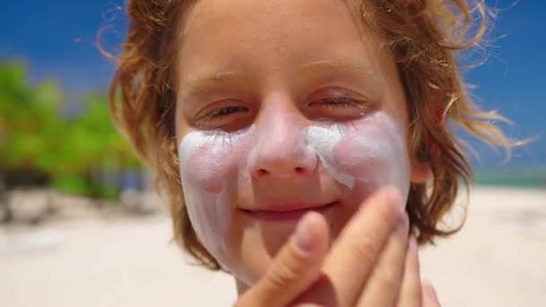 Matka nakłada krem przeciwsłoneczny na twarz małych chłopców na plaży nad morzem. Ochrona przeciwsłoneczna i koncepcja pielęgnacji skóry - Materiał filmowy, wideo