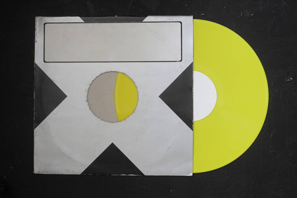 Cubierta de papel negro envejecido y disco LP de vinilo amarillo aislado sobre fondo oscuro - Foto, Imagen