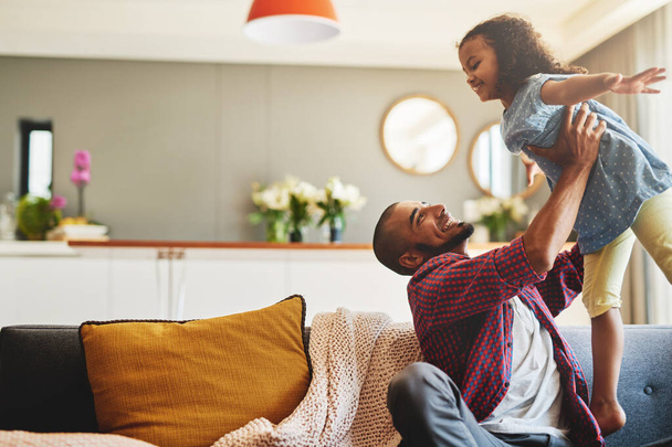 Letting his princess fly. Cropped shot of an affectionate young father lifting his daughter playfully in their living room at home. - 写真・画像