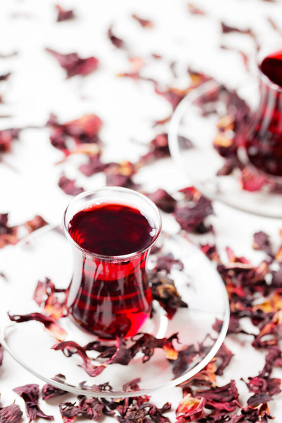 Hibiscus tea in traditional Turkish glasses and dry hibiscus petals. Hibiscus tea on a white background. Close-up - Foto, imagen