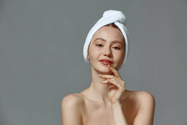 Beautiful young girl with towel on head, clean healthy skin after skincare treatment on gray studio background - Foto, afbeelding