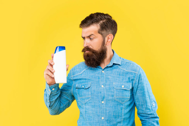 brutal bearded man hold hair conditioner bottle on yellow background, haircare - Foto, imagen