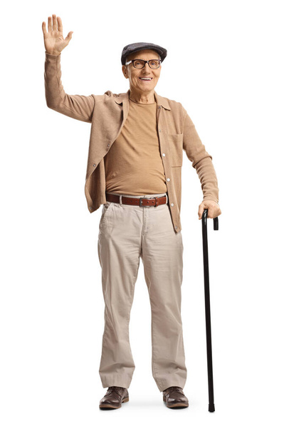 Full length portrait of a smiling elderly gentleman standing with a cane and waving isolated on white background - Φωτογραφία, εικόνα