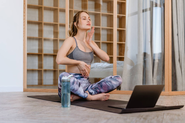 Young white woman using laptop during yoga practice at home - Photo, Image
