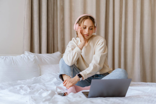 Young woman in headphones using laptop in bedroom at home - Foto, afbeelding