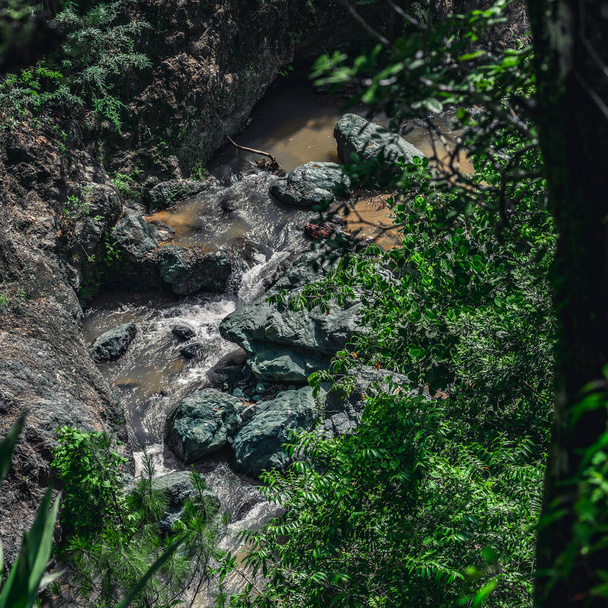 Foto toont een rotsachtige kloof waarin een bergrivier stroomt. De rivier stroomt door enorme blokken stenen. Betoverende wilde dieren van Caribisch eiland verbaast met zijn authenticiteit. Bovenaanzicht van de bergrivier. - Foto, afbeelding