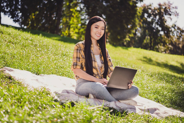 Photo of charming shiny young lady wear checkered shirt smiling sitting grass chatting modern device outdoors urban city park - Φωτογραφία, εικόνα