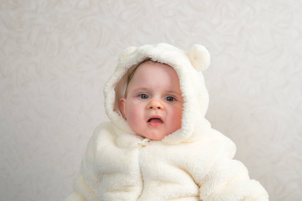 Nettes Baby Mädchen in weißem Pelzmantel lächelt auf glattem Hintergrund. - Foto, Bild