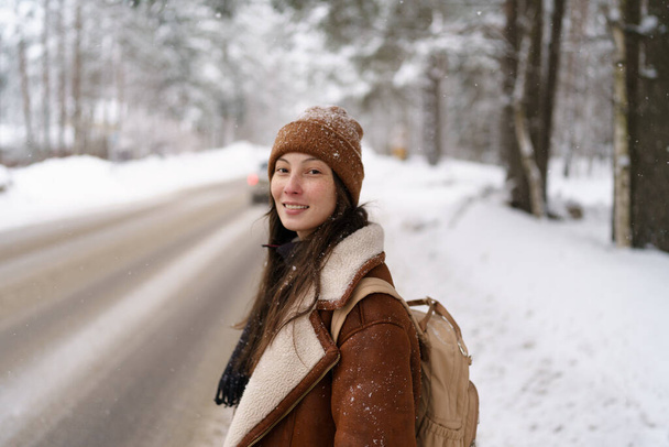 Feliz asiático viajero hitchhiking a lo largo de carretera carretera longitudinalmente nevado bosque de invierno - Foto, Imagen