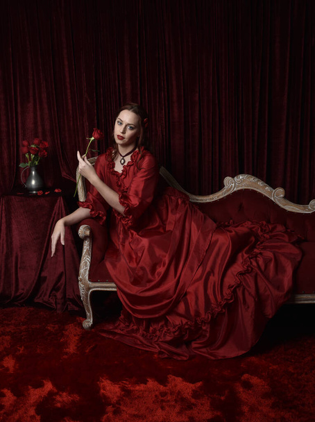  portrét krásné modelky s rezavými vlasy v okouzlujících historických viktoriánských červených plesových šatech. Posing with a moody dark background. - Fotografie, Obrázek