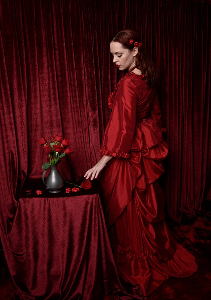  portrait de jolie modèle féminin aux cheveux roux portant une robe de bal victorienne historique glamour. Poser avec un fond sombre et humide. - Photo, image