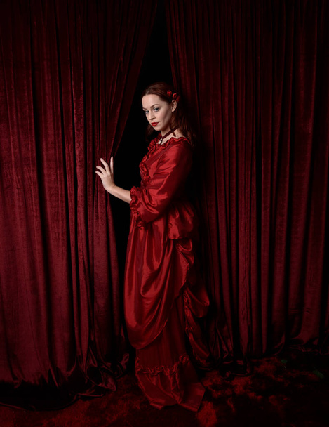  портрет красивої жінки-моделі з червоним волоссям у гламурній історичній вікторіанській червоній сорочці. Позування з приглушеним темним тлом
. - Фото, зображення
