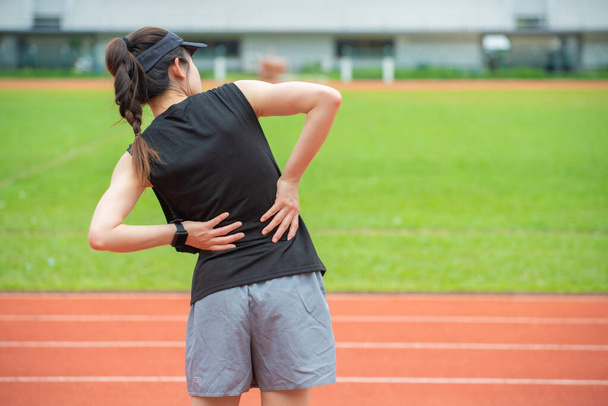 Stadyumdaki koşu pistinde koştuktan sonra sırt ağrısı ya da bel ağrısından muzdarip genç bir koşucunun arka görüntüsü. Spor antrenmanından acı çeken kadın kavramı. - Fotoğraf, Görsel