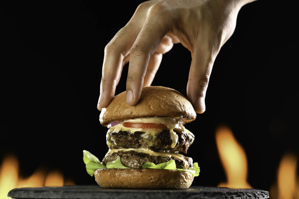 ソースをかけた野菜と肉の二重チーズバーガーにトップバーガーパンを手に入れ、火照りの背景に滴下. - 写真・画像