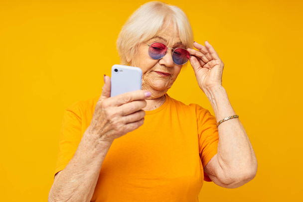 Photo of retired old lady happy lifestyle in yellow t-shirts with phone close-up emotions - Foto, Imagem
