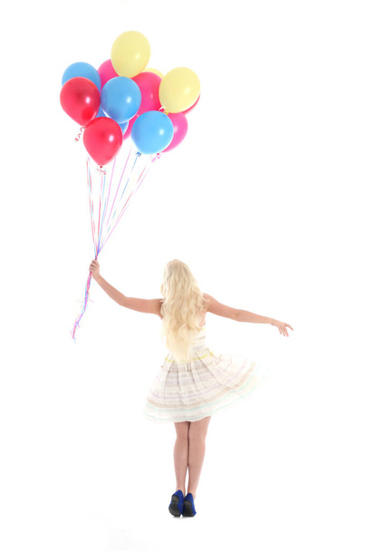 Ganztägiges Porträt eines blonden Mädchens im Partykleid, das ein Bündel bunter Luftballons in der Hand hält. Isoliert auf weißem Studiohintergrund - Foto, Bild