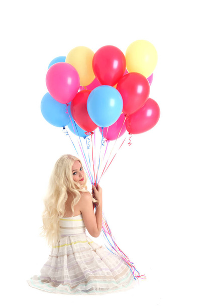 Full length portrait of blonde girl wearing party dress, holding bunch of colourful balloons. Isolated on white studio background - 写真・画像