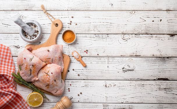 Sliced chicken thighs with skin on a cutting board. White wooden background. Top view. Copy space - Φωτογραφία, εικόνα