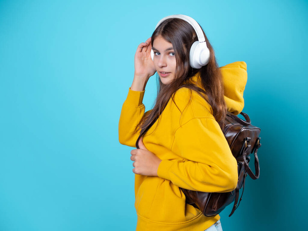 A young smiling student with a backpack and headphones, listening to music or recording a lecture. - Foto, afbeelding